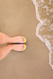 Photo of Top view of woman with stylish flip flops on sand near sea, space for text. Beach accessories