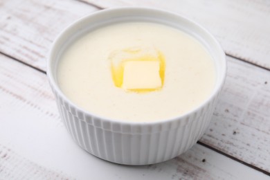 Photo of Bowl of delicious semolina pudding with butter on white wooden table, closeup