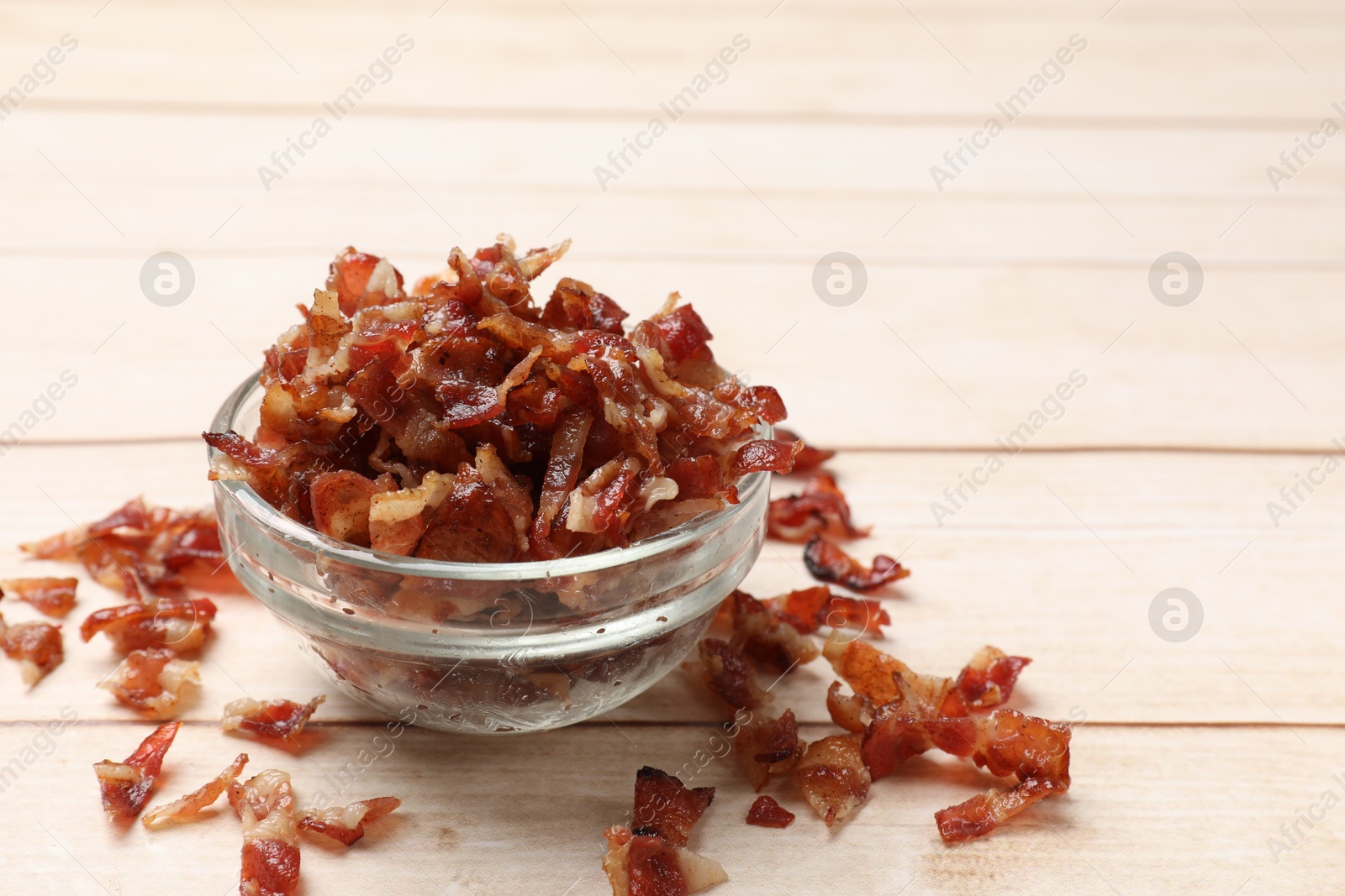 Photo of Pieces of tasty fried bacon in bowl on wooden table, closeup. Space for text