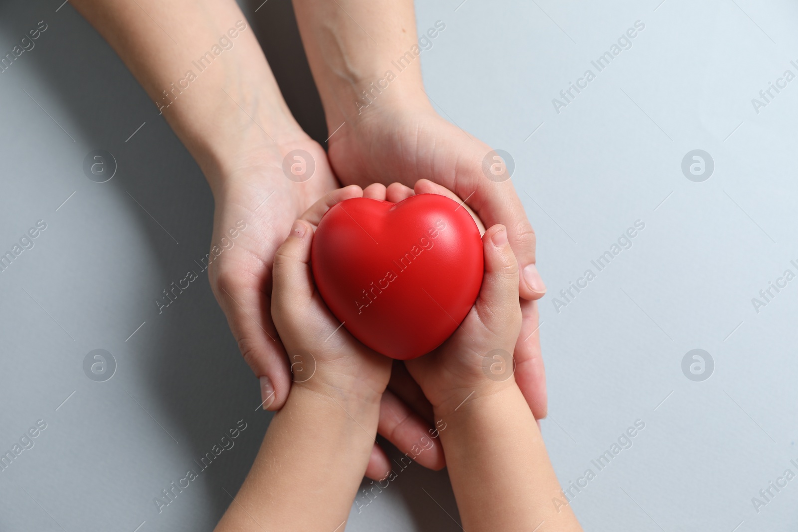 Photo of Mother and her child holding red decorative heart on gray background, top view