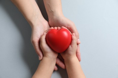 Photo of Mother and her child holding red decorative heart on gray background, top view