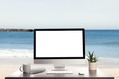 Image of Modern computer with blank screen on table and view of beautiful seascape