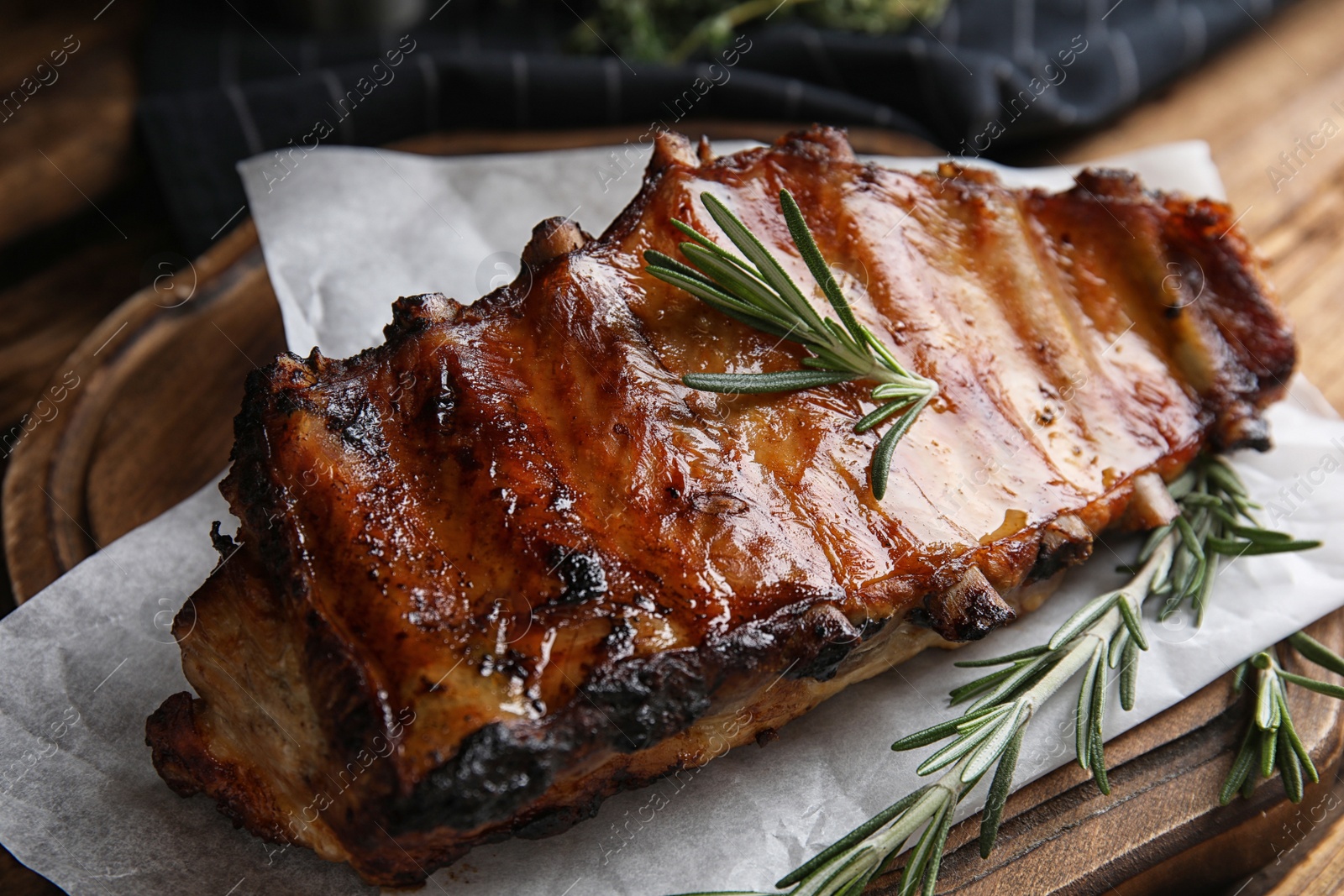 Photo of Tasty grilled ribs with rosemary on wooden board, closeup