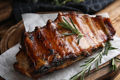 Photo of Tasty grilled ribs with rosemary on wooden board, closeup