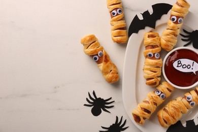Photo of Flat lay composition with tasty sausage mummies for Halloween party on white marble table. Space for text