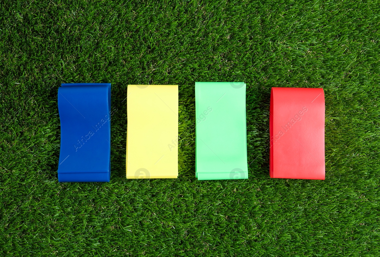 Photo of Fitness elastic bands on green grass, flat lay