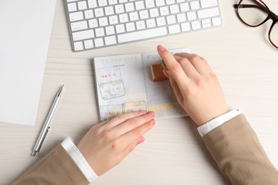 Photo of Ukraine, Lviv - September 6, 2022: Woman stamping visa page in passport at white wooden table, top view