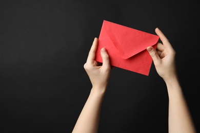 Woman holding red paper envelope on black background, closeup