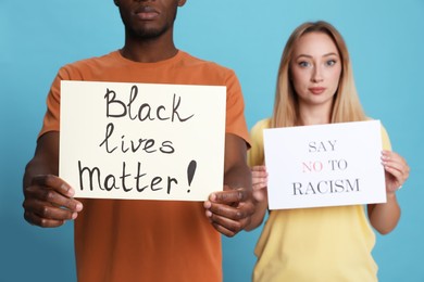 Photo of Young woman and African American man holding signs on light blue background, closeup. Racism concept