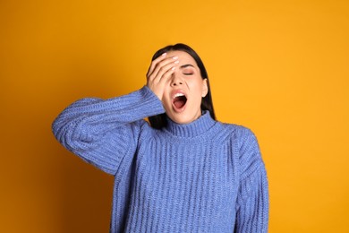 Young tired woman yawning on yellow background