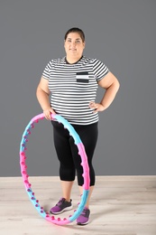 Overweight woman with hula hoop against gray wall