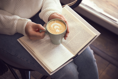 Photo of Woman with cup of coffee reading book indoors, closeup