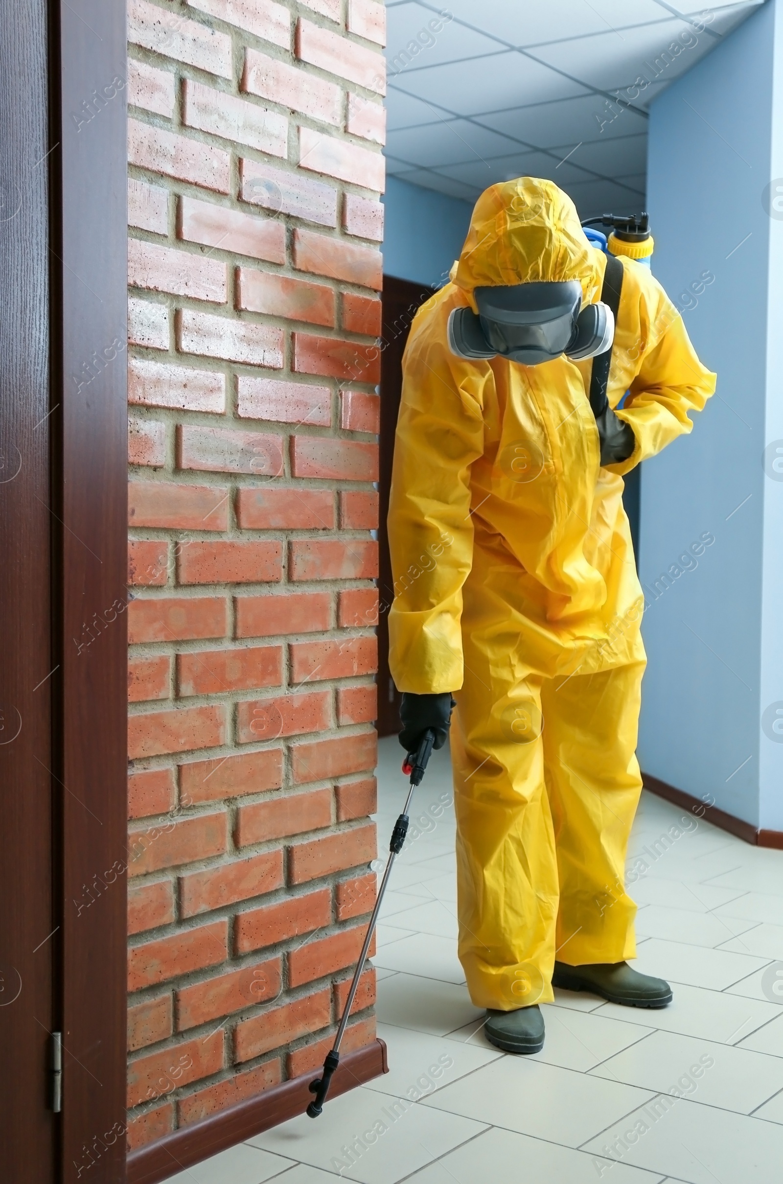 Photo of Pest control worker in protective suit spraying pesticide indoors