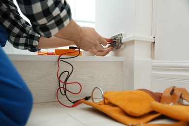 Electrician with screwdriver repairing power socket indoors, closeup