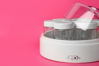 Modern yogurt maker with empty jars on pink background, closeup. Space for text