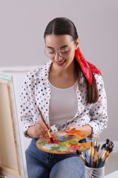 Happy woman artist drawing picture on canvas indoors