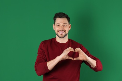 Photo of Portrait of handsome man making heart with his hands on color background