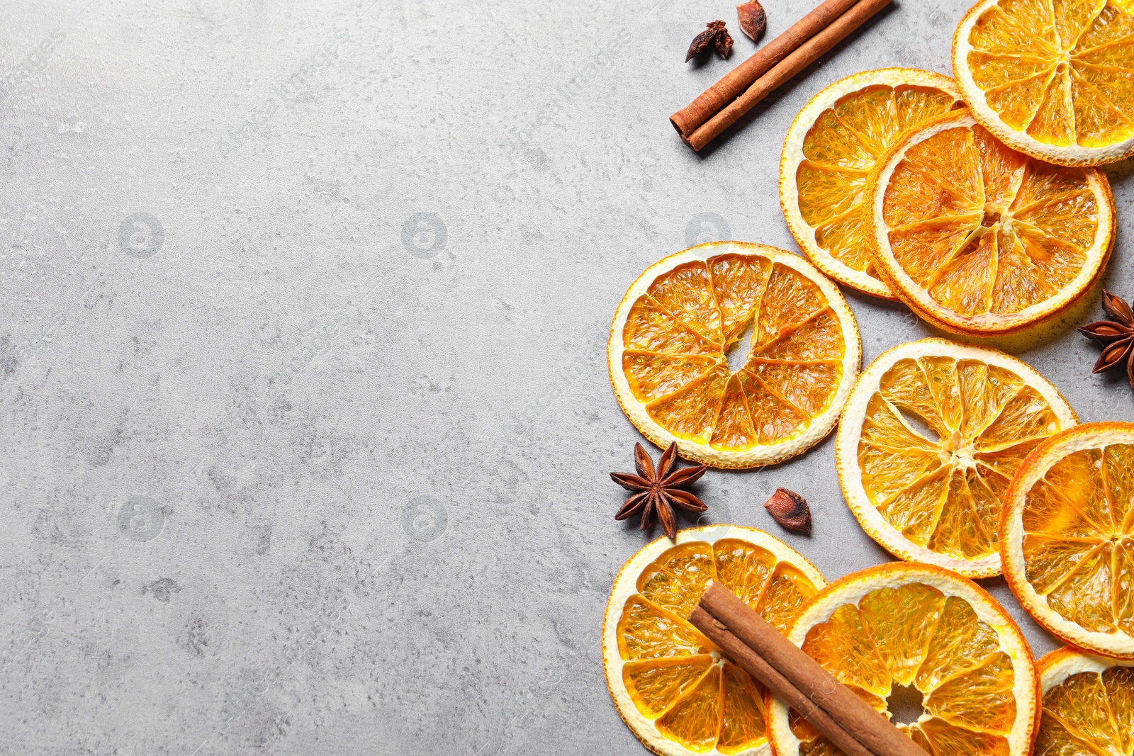 Photo of Dry orange slices, cinnamon sticks and anise stars on grey table, flat lay. Space for text