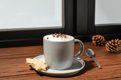 Photo of Cup of cappuccino with cookies on windowsill indoors. Winter drink