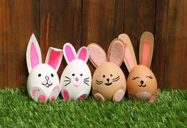 Easter eggs as cute bunnies on green grass against wooden background