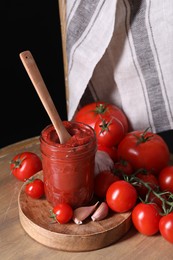 Jar of tasty tomato paste with spoon and ingredients on wooden table