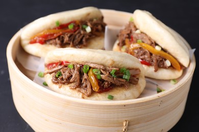 Photo of Delicious gua bao in bamboo steamer on black table, closeup