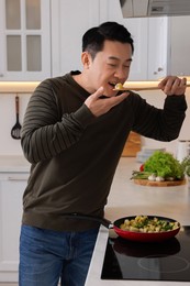 Photo of Cooking process. Man tasting potato in kitchen