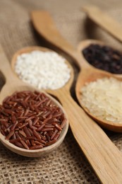 Spoons with different sorts of rice on burlap fabric, closeup