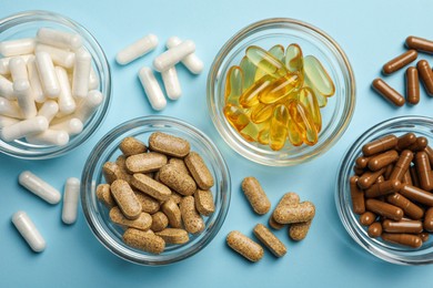 Different dietary supplements on light blue background, flat lay