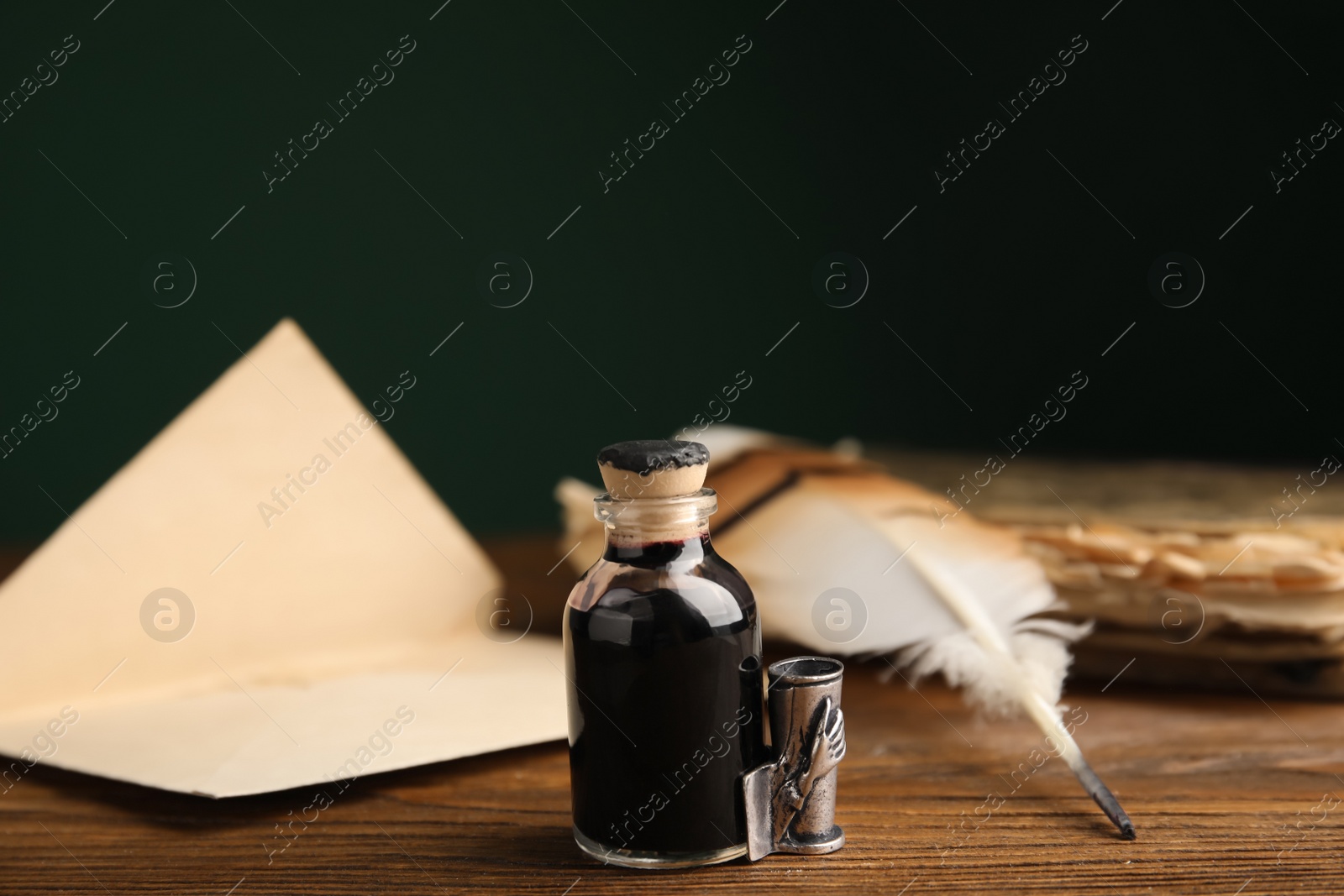 Photo of Feather pen, bottle of ink and old paper on wooden table