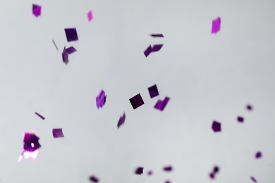 Shiny purple confetti falling down on light grey background