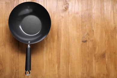 Photo of Empty iron wok on wooden table top view. Space for text