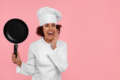 Photo of Emotional female chef in uniform holding frying pan on pink background. Space for text