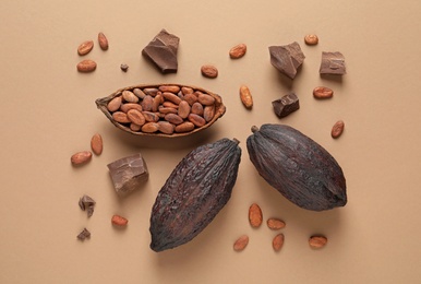 Photo of Cocoa pods with beans and chocolate pieces on light brown background, flat lay