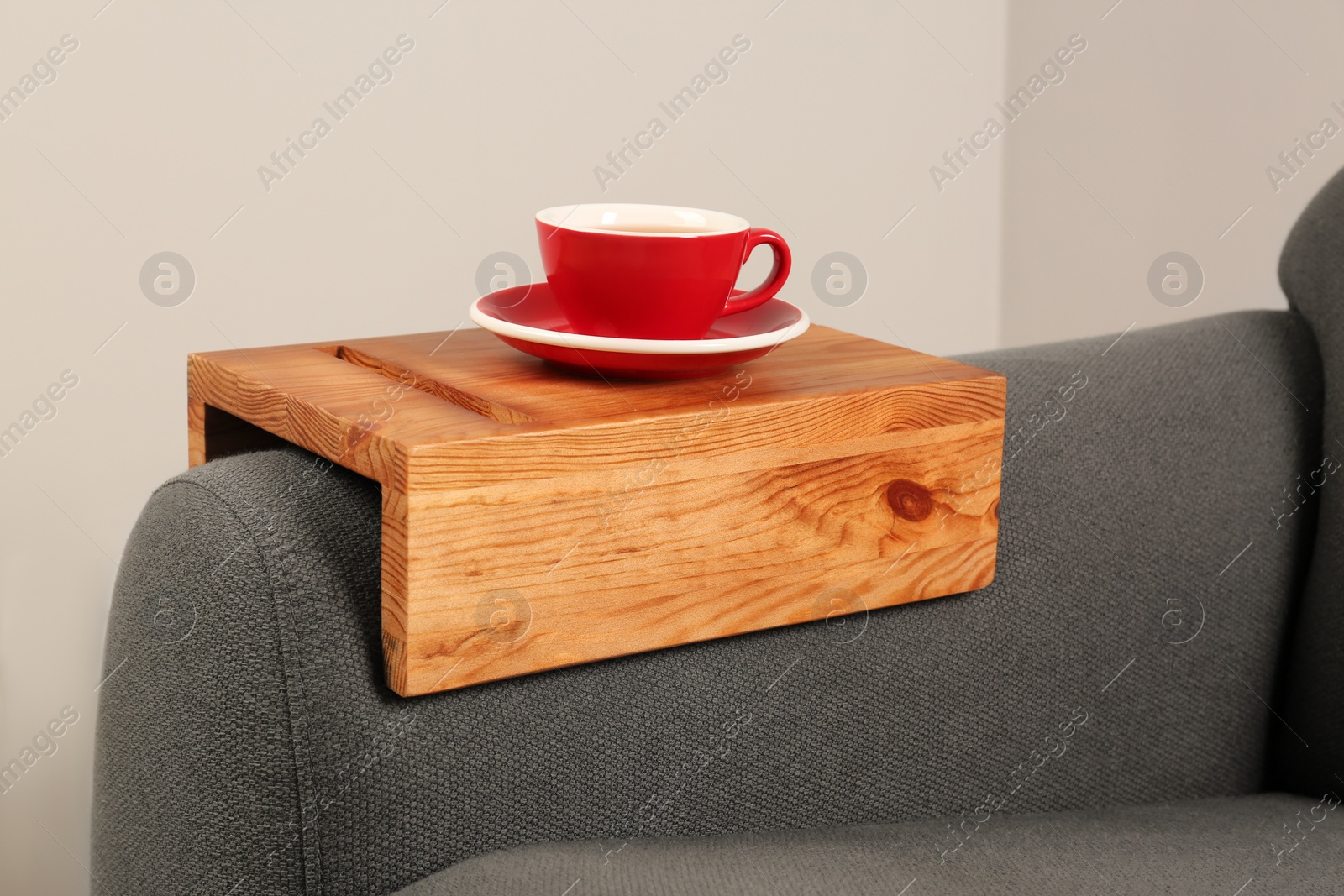 Photo of Cup of tea on sofa with wooden armrest table in room. Interior element