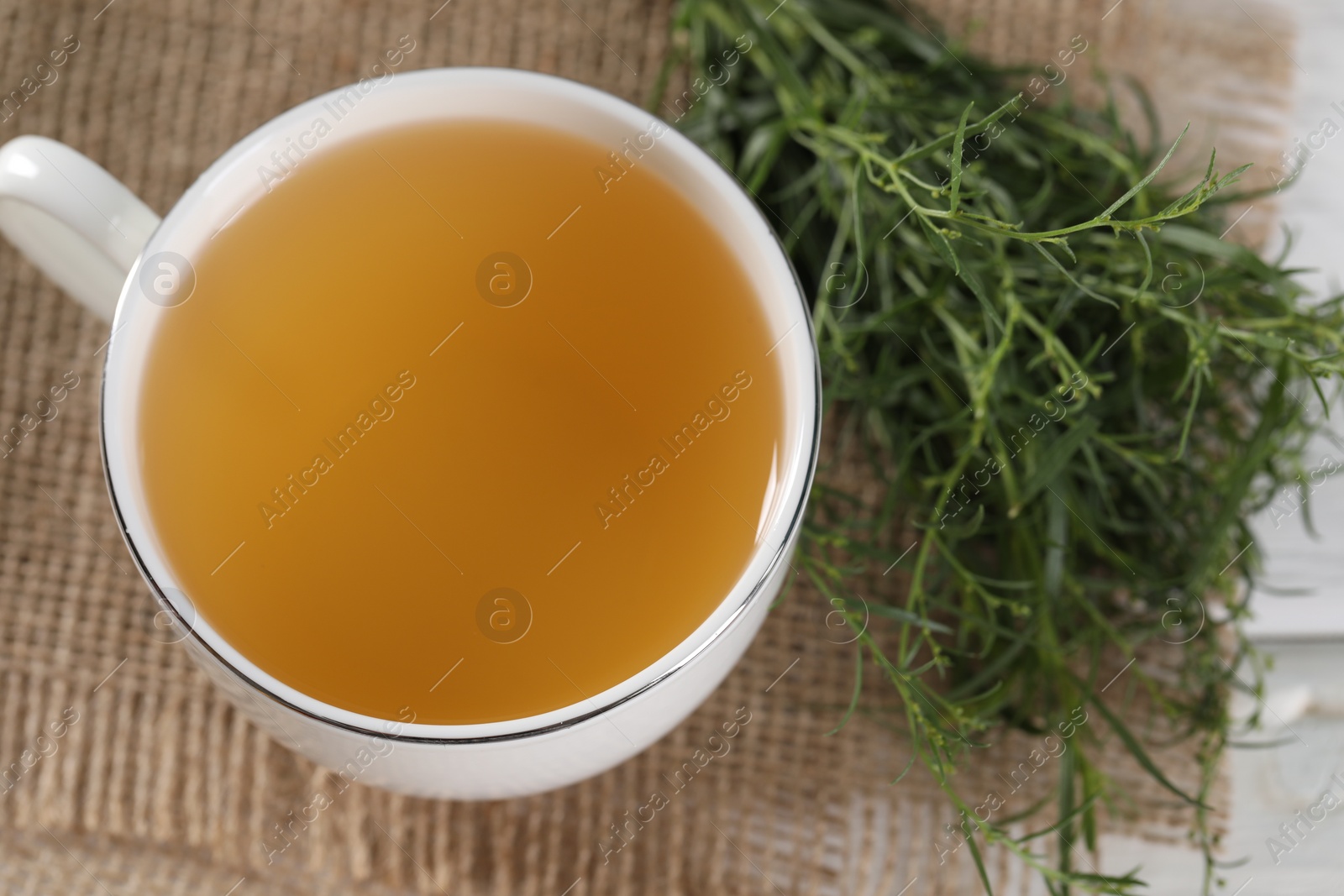 Photo of Aromatic herbal tea and fresh tarragon sprigs on table, above view