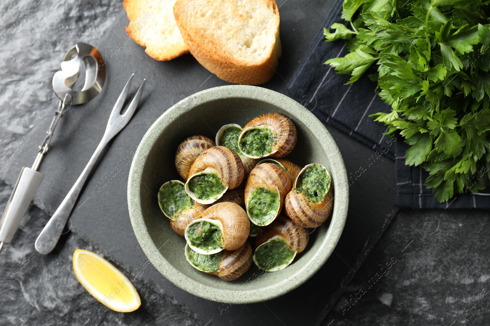 Photo of Delicious cooked snails served on grey textured table, flat lay