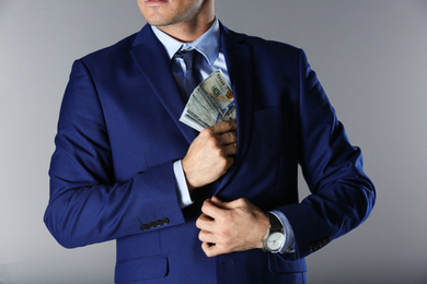 Man putting bribe into pocket on grey background, closeup