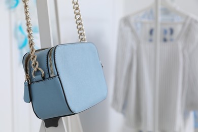 Elegant light blue handbag hanging on rack in dressing room