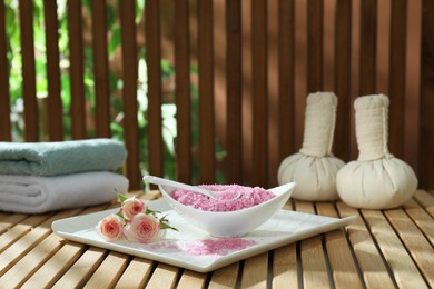 Bowl of pink sea salt and beautiful roses on wooden table, space for text