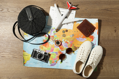 World map and items on wooden background, flat lay. Travel during summer vacation