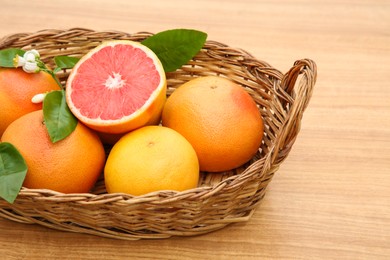 Photo of Wicker basket with fresh ripe grapefruits and green leaves on wooden table