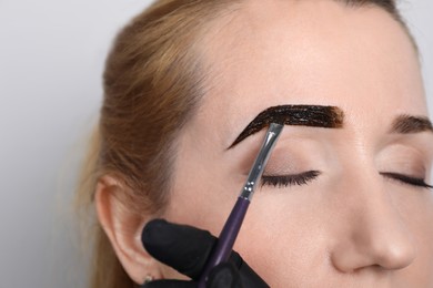 Photo of Beautician applying tint during eyebrows correction procedure on light grey background, closeup