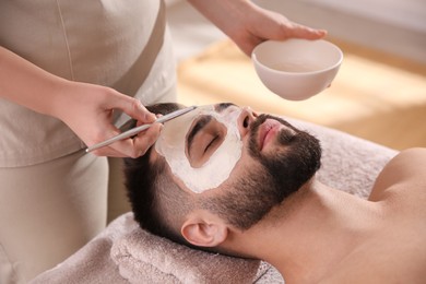 Cosmetologist applying mask on man's face in spa salon