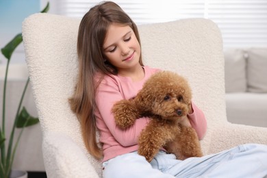 Little child with cute puppy in armchair at home. Lovely pet