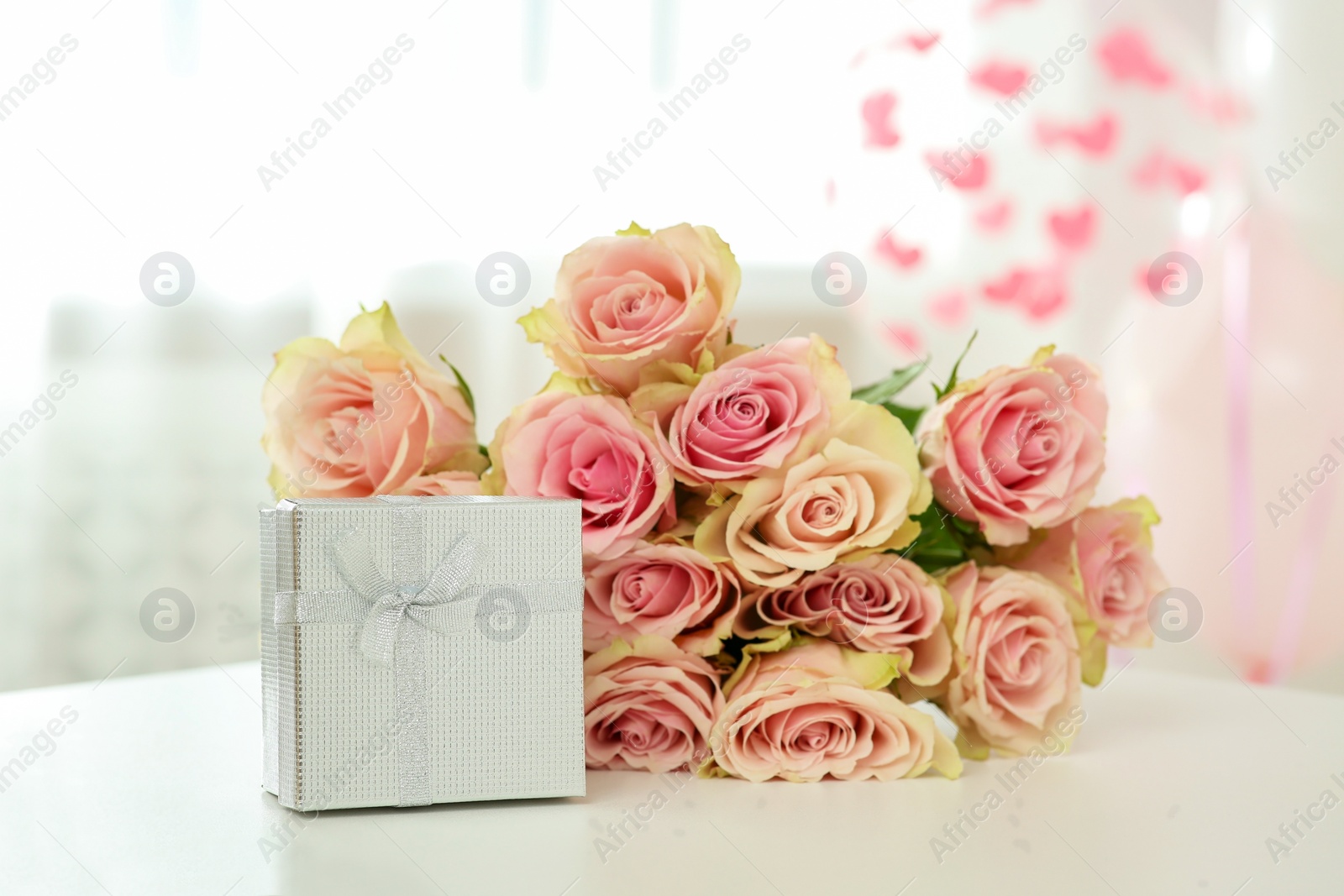 Photo of Beautiful bouquet of roses and gift on white table in room. Happy birthday greetings