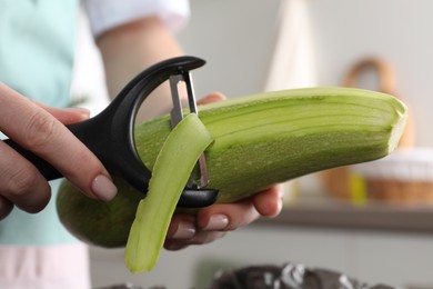 Photo of Woman peeling fresh zucchini in kitchen, closeup