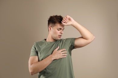 Photo of Young man with sweat stain on his clothes against beige background. Using deodorant