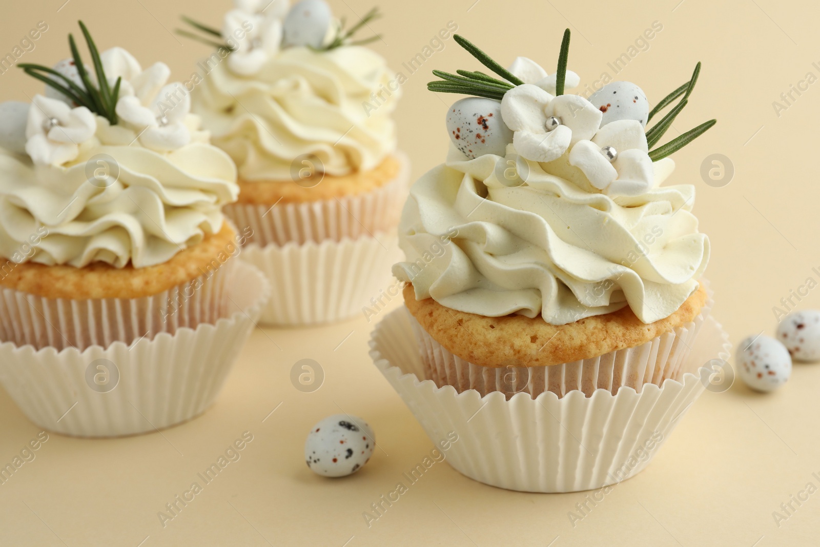 Photo of Tasty Easter cupcakes with vanilla cream and candies on beige background, closeup