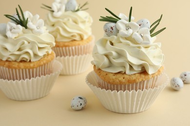 Photo of Tasty Easter cupcakes with vanilla cream and candies on beige background, closeup